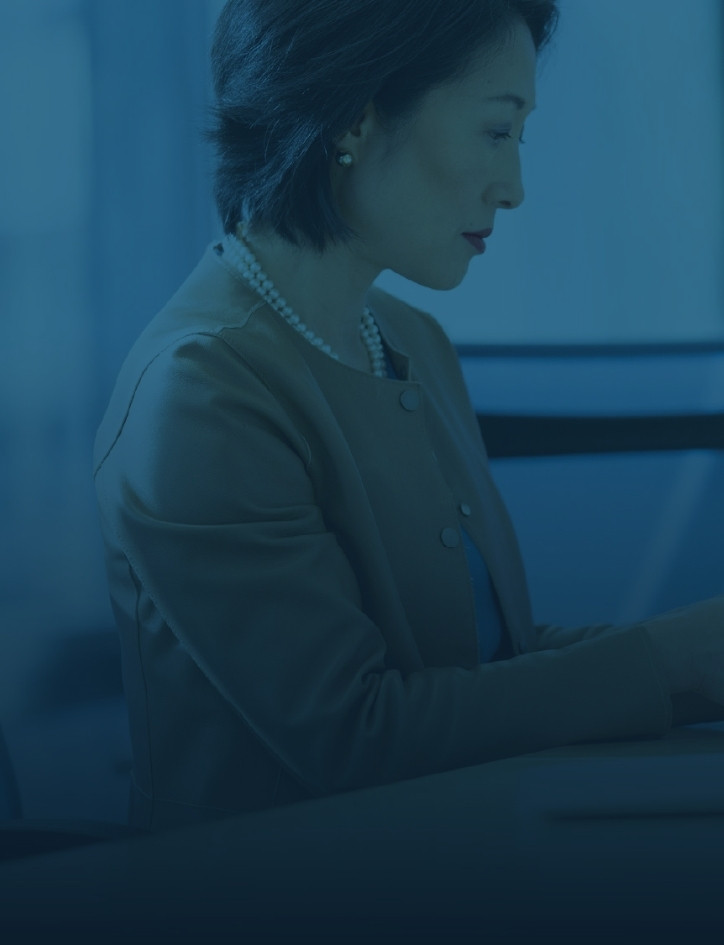 A business woman seated in an office looking down with a blue tint over the image