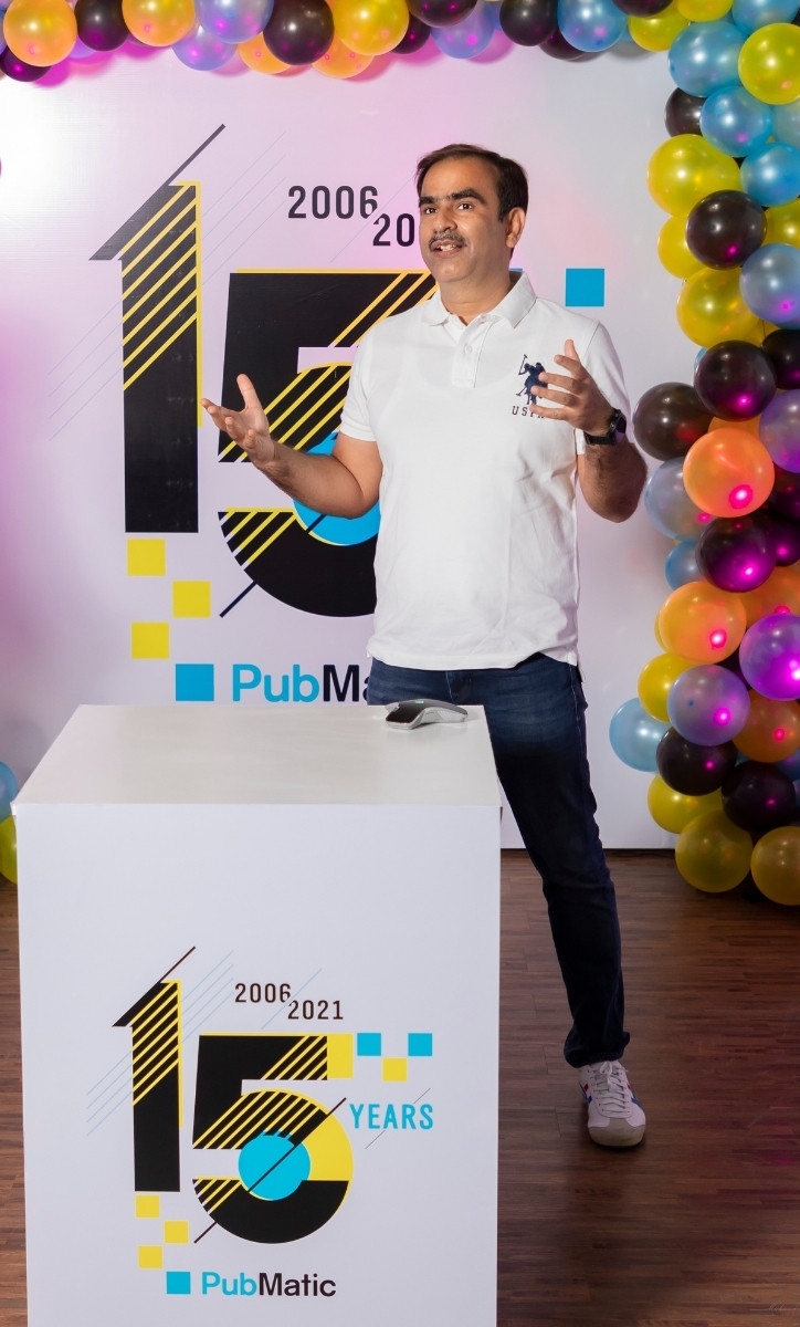Adult man standing on stage with a podium in front of him. There are yellow, black, and blue ballons in front of him.