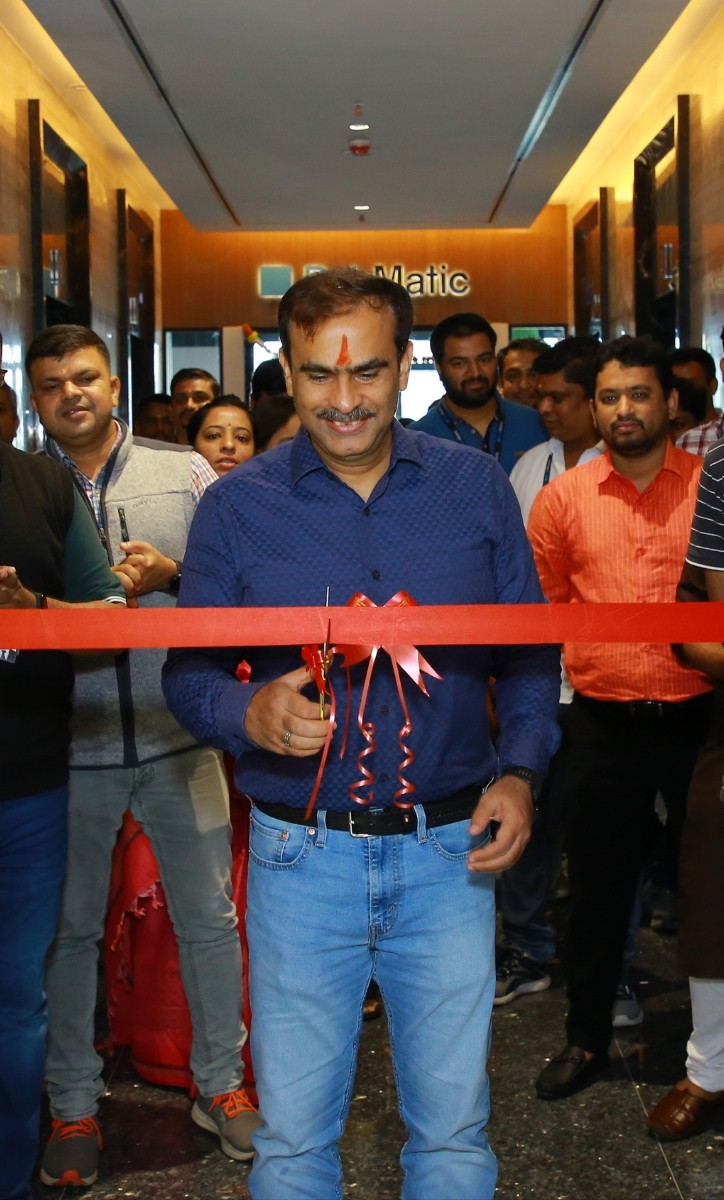 A smiling man standing in front of a crowd cutting a ribbon
