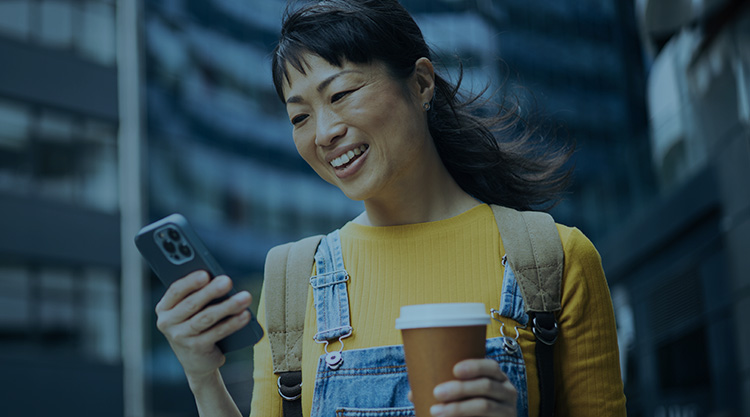 A woman with coffee smiles as she looks at her mobile device